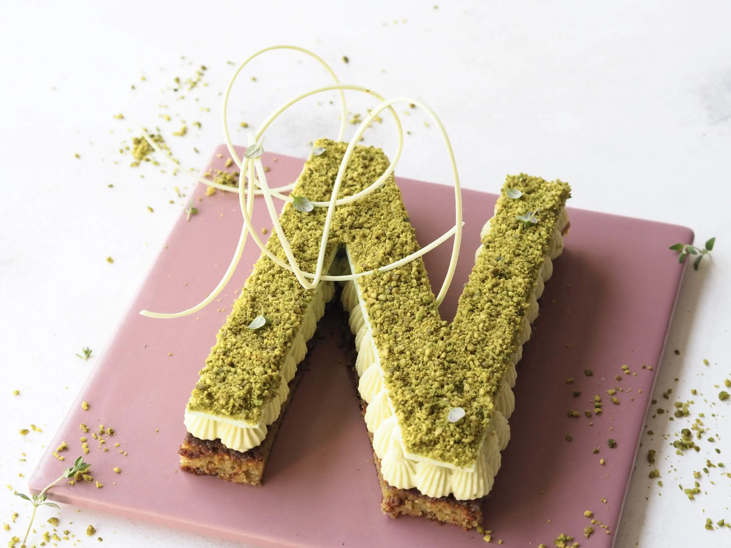 Tal- og bogstavskage sprøjtet op med en stikkelsbærcreme og pyntet med et chokoladelåg og pistacie